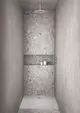 Dusche mit runder Kopfbrause und Wandverkleidung aus grauem Stein. Im Hintergrund befinden sich einige Pflegeprodukte. Ideal Standard ist der Hersteller.
